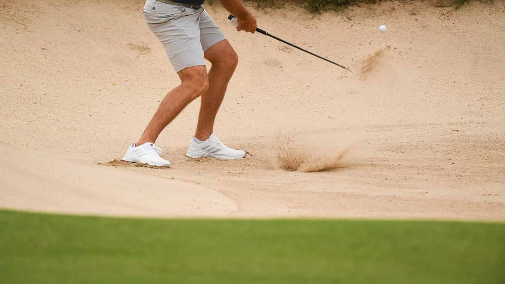 A golfer having shot in bunker holding a golf wedge from sands